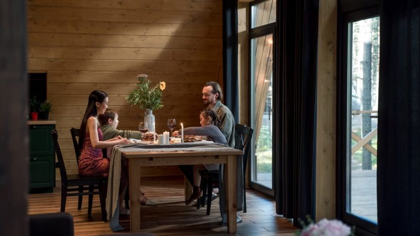 A family enjoying dinner in a cozy, modern wooden cabin with warm lighting.